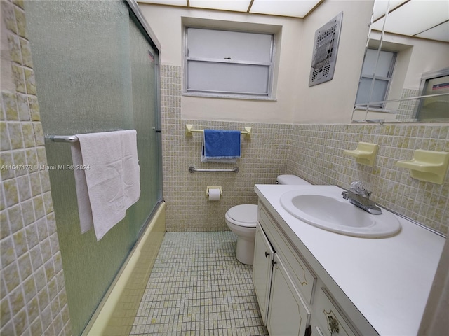 full bathroom with tile walls, tile patterned flooring, combined bath / shower with glass door, vanity, and toilet