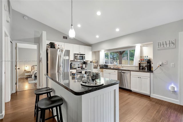 kitchen with vaulted ceiling, appliances with stainless steel finishes, hardwood / wood-style flooring, and white cabinets