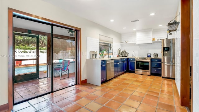 kitchen with appliances with stainless steel finishes, sink, light tile patterned flooring, blue cabinets, and tasteful backsplash