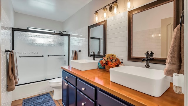 full bathroom with vanity, toilet, bath / shower combo with glass door, and tile walls