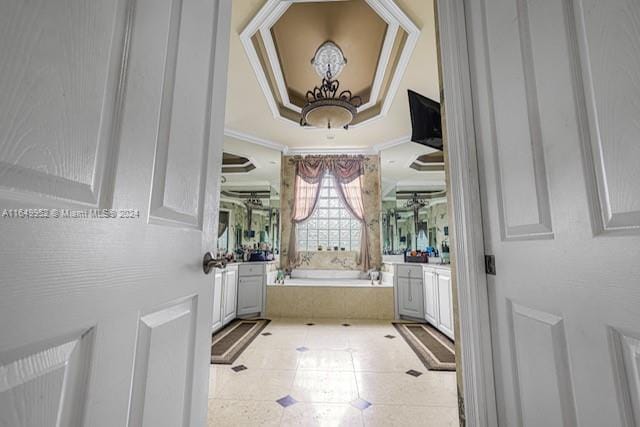 interior space with tile patterned floors, a raised ceiling, vanity, tiled bath, and ornamental molding