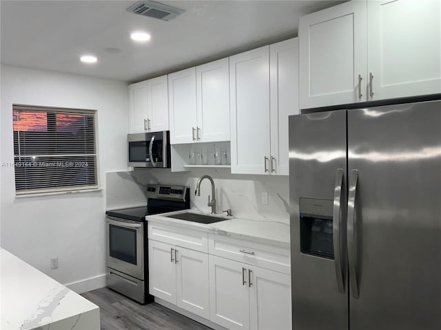 kitchen with wood-type flooring, tasteful backsplash, stainless steel appliances, sink, and white cabinets