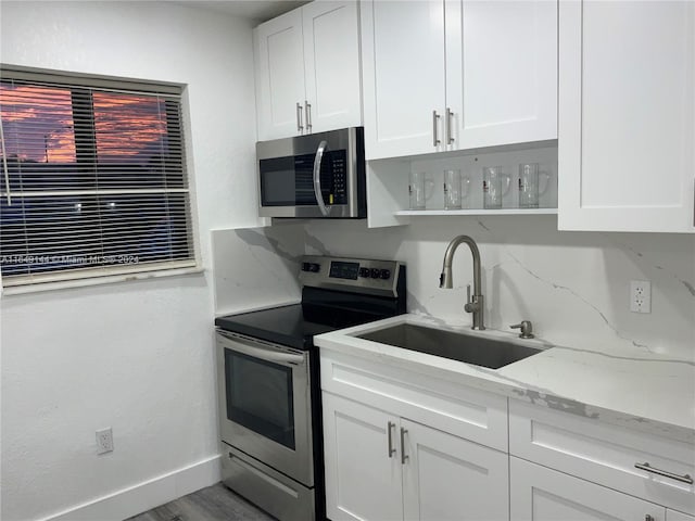 kitchen with hardwood / wood-style floors, stainless steel appliances, sink, light stone countertops, and white cabinets