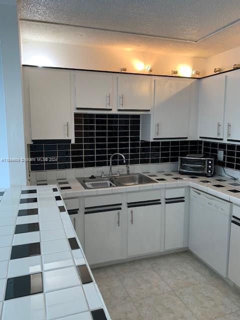 kitchen with tasteful backsplash, light tile patterned floors, dishwasher, sink, and white cabinets