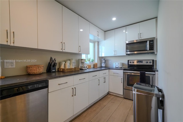 kitchen with appliances with stainless steel finishes, white cabinetry, and light hardwood / wood-style flooring