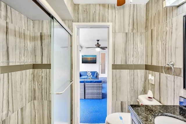 bathroom featuring tile walls, ceiling fan, toilet, and a shower with shower door