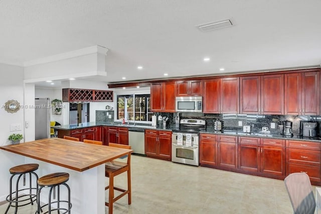 kitchen with a breakfast bar area, appliances with stainless steel finishes, kitchen peninsula, decorative backsplash, and wooden counters