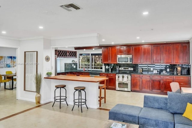 kitchen featuring tasteful backsplash, a kitchen bar, stainless steel appliances, ornamental molding, and kitchen peninsula