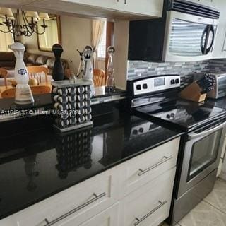 kitchen featuring appliances with stainless steel finishes, light tile patterned floors, white cabinets, and a notable chandelier