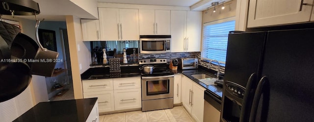 kitchen with backsplash, appliances with stainless steel finishes, white cabinetry, track lighting, and light tile patterned flooring