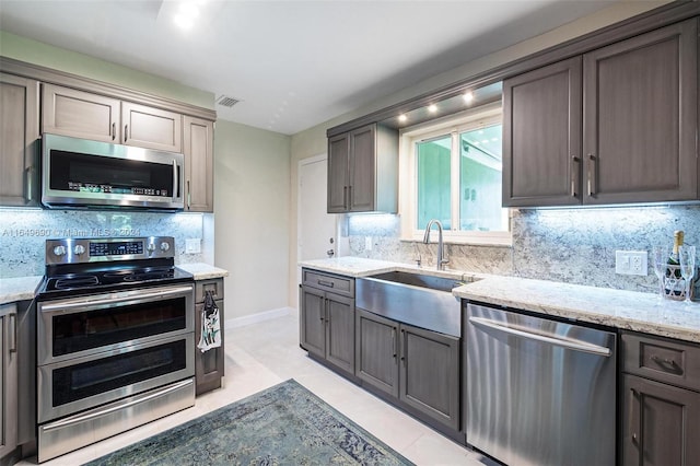 kitchen featuring light stone countertops, stainless steel appliances, decorative backsplash, and light tile patterned flooring