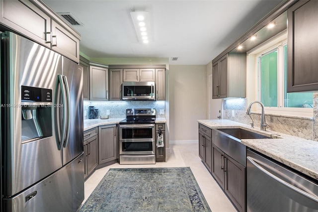 kitchen featuring stainless steel appliances, light stone counters, sink, decorative backsplash, and light tile patterned flooring