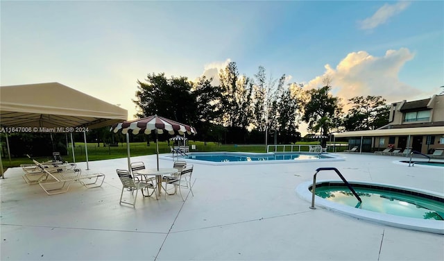 pool at dusk featuring a community hot tub and a patio area