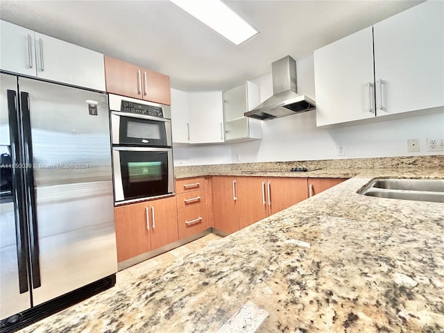 kitchen with wall chimney range hood, appliances with stainless steel finishes, white cabinetry, and light stone countertops