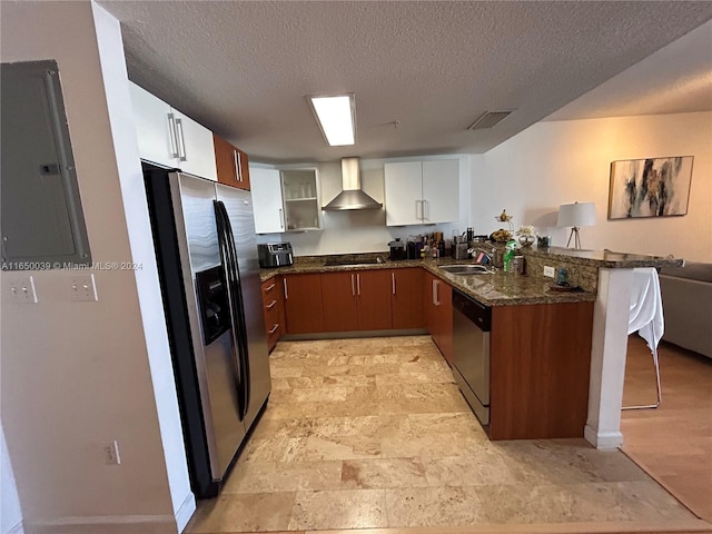 kitchen with dark stone counters, kitchen peninsula, sink, appliances with stainless steel finishes, and wall chimney range hood