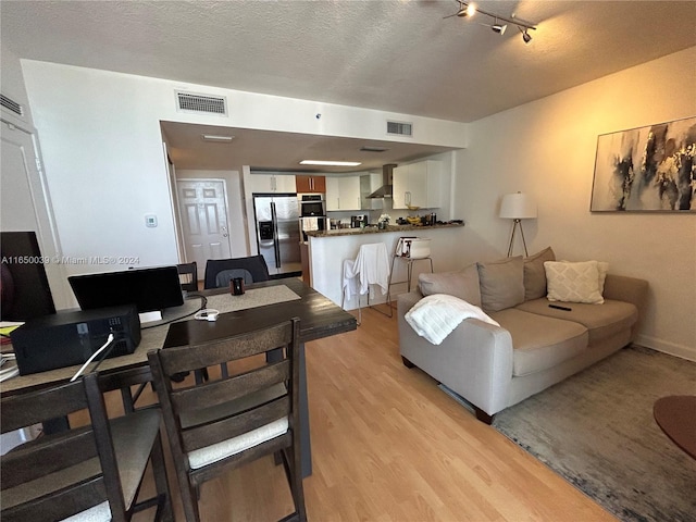 living room with a textured ceiling, light hardwood / wood-style flooring, and rail lighting