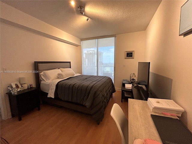 bedroom featuring track lighting, a wall of windows, a textured ceiling, access to outside, and dark wood-type flooring