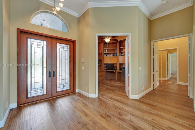 entrance foyer with crown molding, a towering ceiling, light wood-type flooring, and french doors