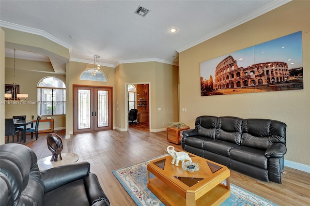 living room featuring light wood-type flooring, ornamental molding, an inviting chandelier, and french doors