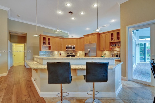 kitchen with hanging light fixtures, stainless steel appliances, light wood-type flooring, and decorative backsplash