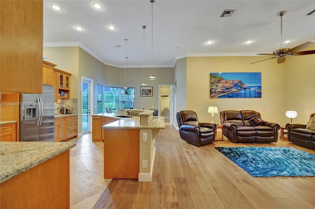 kitchen featuring stainless steel fridge with ice dispenser, hanging light fixtures, ceiling fan, light stone counters, and light wood-type flooring