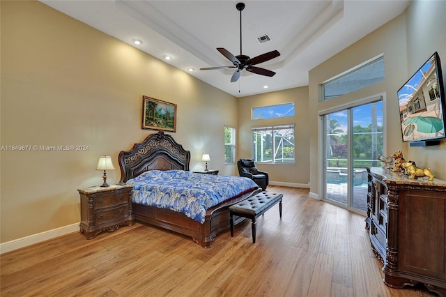 bedroom with a high ceiling, light hardwood / wood-style flooring, access to exterior, ceiling fan, and a tray ceiling