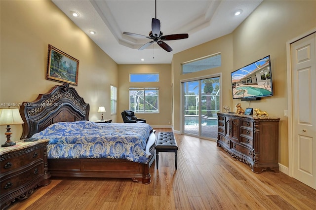 bedroom featuring a tray ceiling, ceiling fan, light hardwood / wood-style floors, and access to outside