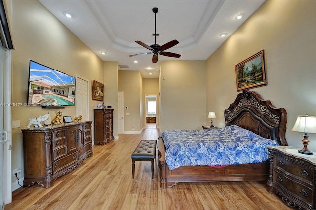 bedroom featuring ceiling fan, light wood-type flooring, and a tray ceiling