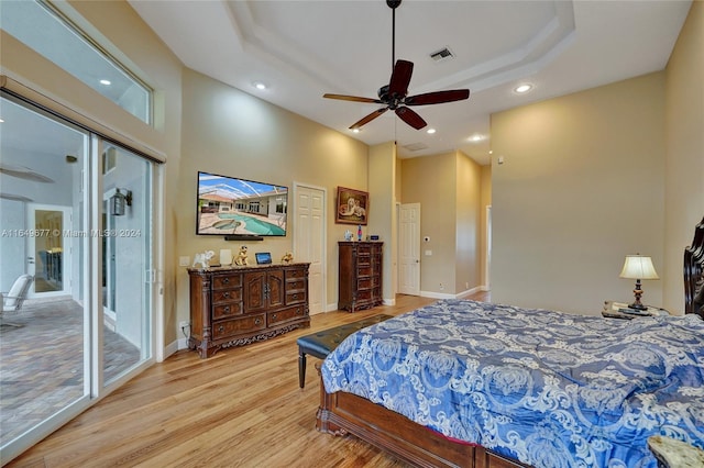 bedroom featuring light hardwood / wood-style flooring, a tray ceiling, access to exterior, ceiling fan, and multiple windows