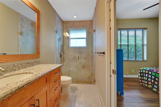 bathroom with a shower with shower door, vanity, hardwood / wood-style floors, toilet, and ceiling fan