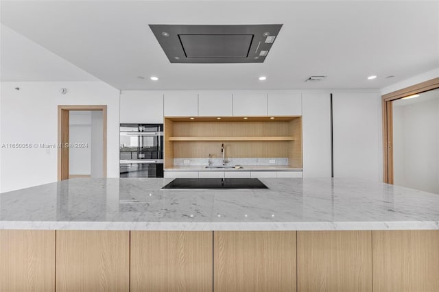 kitchen with light brown cabinets, black appliances, white cabinets, sink, and light stone countertops