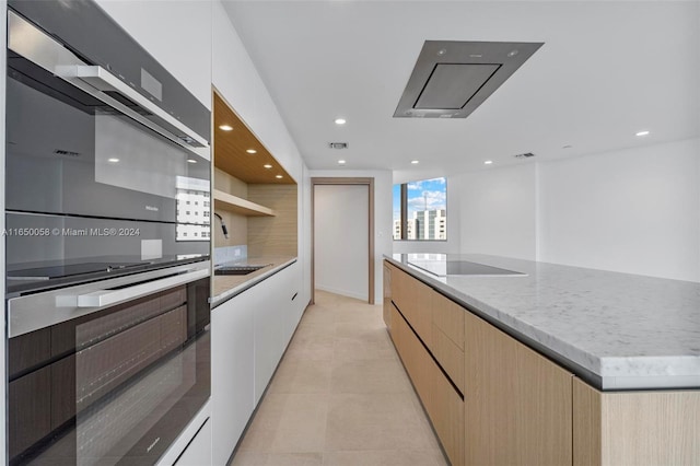 kitchen featuring light brown cabinets, light tile patterned floors, a kitchen island, white cabinets, and black appliances