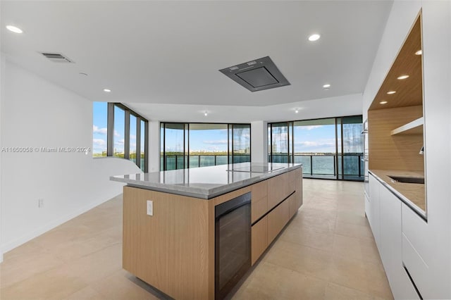 kitchen with floor to ceiling windows, beverage cooler, a spacious island, a water view, and white cabinets