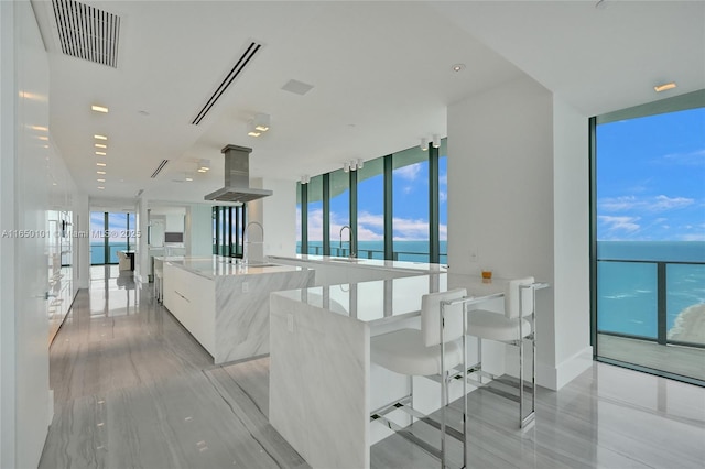 kitchen with a large island with sink, sink, island exhaust hood, a water view, and white cabinets