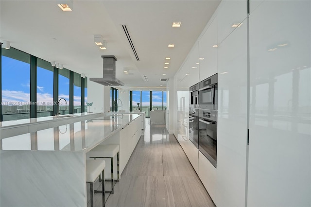 19575 Collins Ave Unit 33, Sunny Isles Beach, FL 33160 - kitchen with modern cabinets, island range hood, white cabinetry, a wall of windows, and a sink