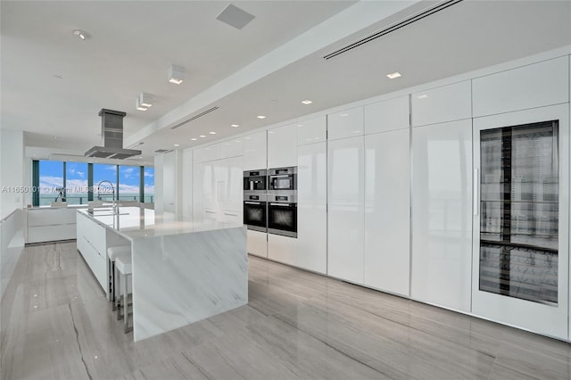 kitchen with white cabinetry, island exhaust hood, a kitchen island with sink, a breakfast bar, and sink