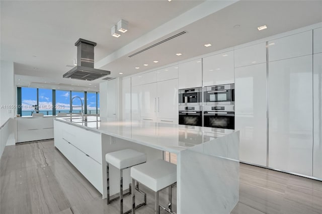 kitchen featuring white cabinetry, island range hood, a large island, and stainless steel double oven