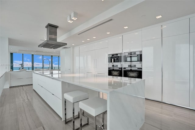 19575 Collins Ave Unit 33, Sunny Isles Beach, FL 33160 - kitchen featuring modern cabinets, stainless steel double oven, island exhaust hood, white cabinets, and a wall of windows