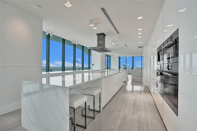 kitchen with white cabinetry, floor to ceiling windows, island range hood, a large island, and stainless steel oven