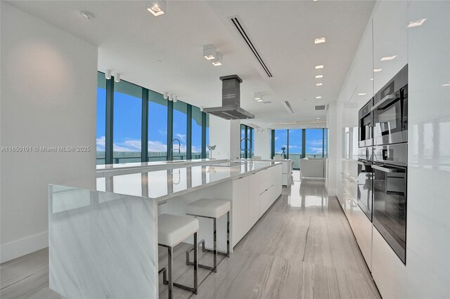 19575 Collins Ave Unit 33, Sunny Isles Beach, FL 33160 - kitchen featuring modern cabinets, white cabinets, island range hood, a spacious island, and black oven