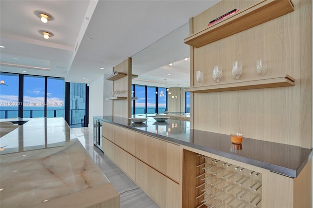 kitchen with a water view, a wall of windows, light brown cabinets, and a healthy amount of sunlight