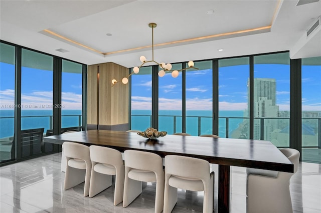 dining room with a wealth of natural light, a tray ceiling, a wall of windows, and a water view