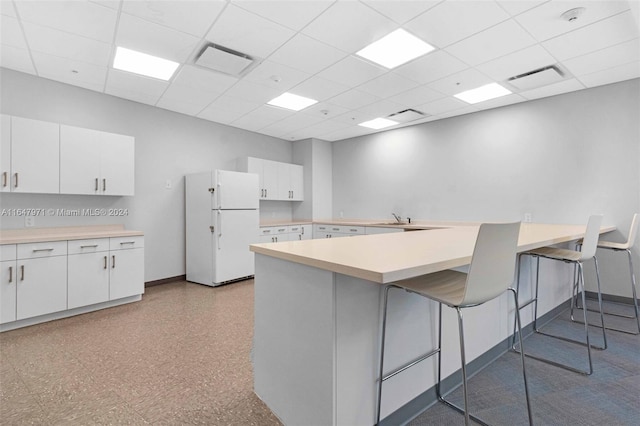 kitchen featuring a paneled ceiling, white fridge, a kitchen bar, and kitchen peninsula