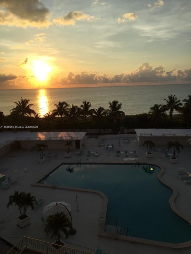 pool at dusk with a water view and a patio area