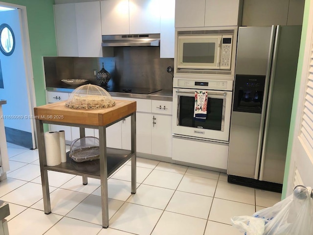 kitchen featuring tasteful backsplash, white cabinetry, light tile patterned flooring, and white appliances