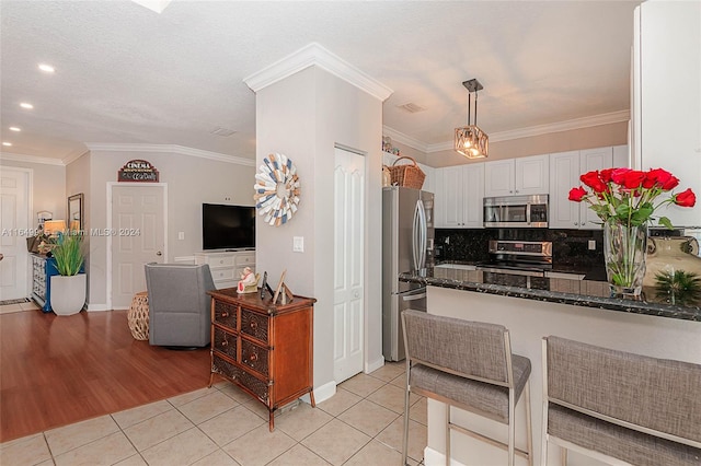 kitchen with stainless steel appliances, ornamental molding, white cabinets, and light tile patterned flooring