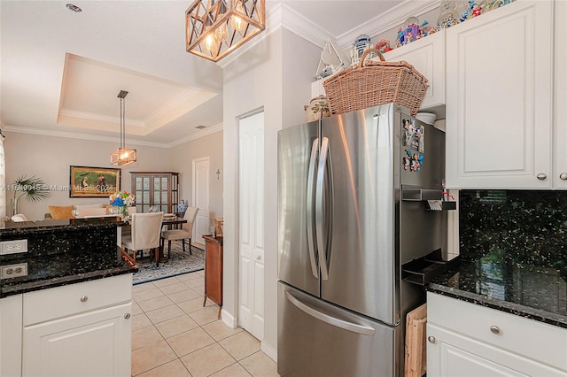 kitchen featuring a tray ceiling, dark stone counters, stainless steel refrigerator, and white cabinets