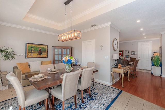 dining area with a tray ceiling, light hardwood / wood-style floors, a chandelier, and ornamental molding