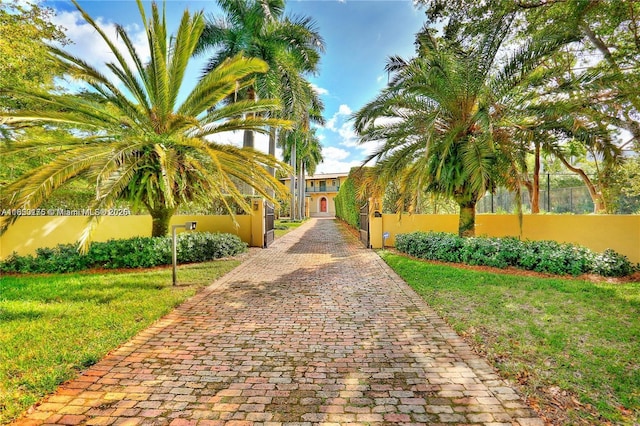 view of property's community featuring a lawn, decorative driveway, and fence