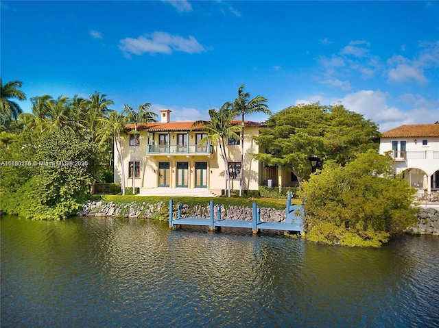 back of property with stucco siding, a water view, and a balcony